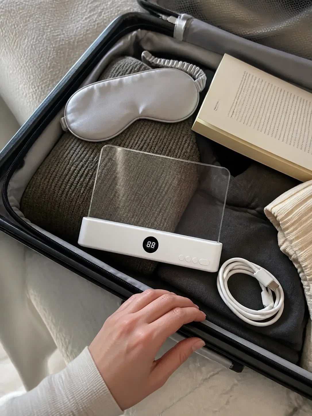 White Lumalli packed in a carry-on with a book and charging cable
